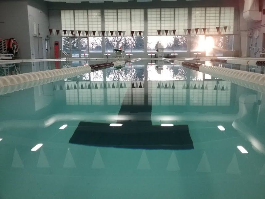 Indoor swimming pool with lane markers and starting blocks, illuminated by sunlight coming through large windows.